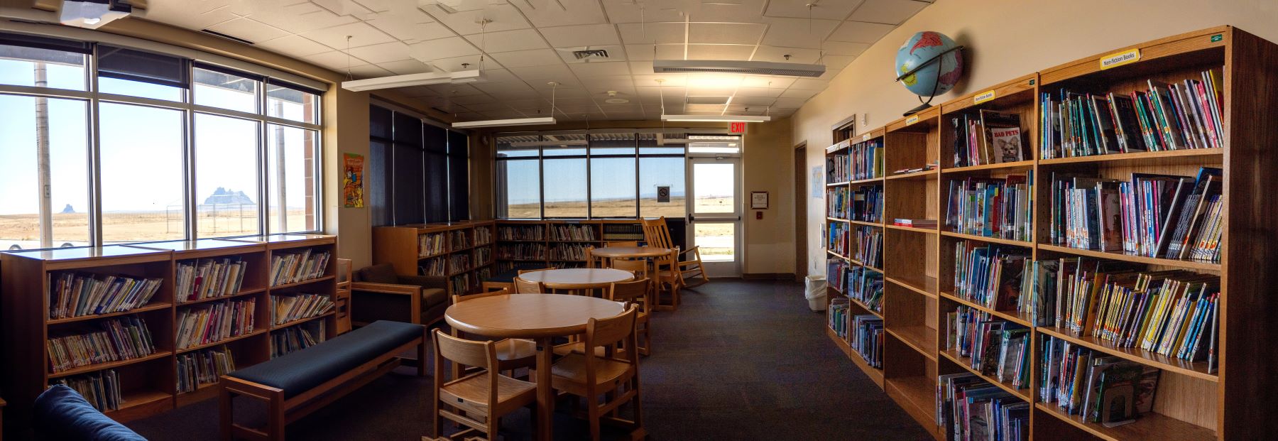 A cozy library featuring tables and chairs arranged by a large window, perfect for reading or studying.
