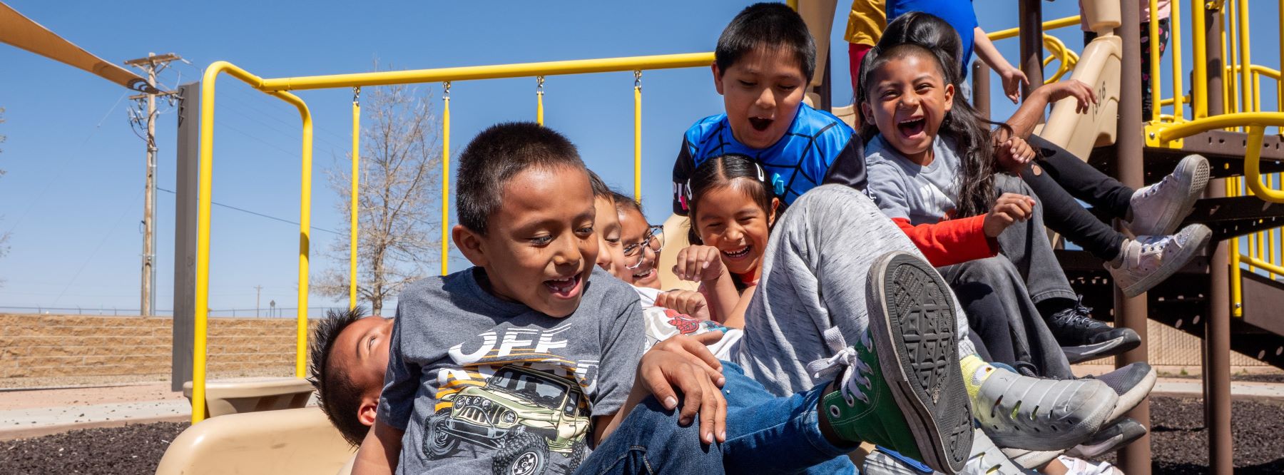 Students enjoying a fun time on a playground slide, smiling and playing together in a bright outdoor setting.