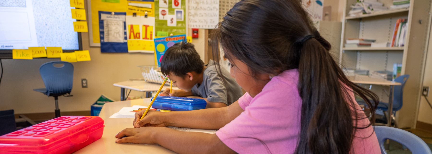 Two students busy writing at a desk in a classroom.